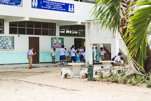 Full length view of elementary-age children in uniforms with backpacks walking towards building entrance and two of their instructors.