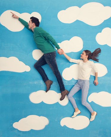Young couple in a cartoon, directly above shot. Girl and boy on clouds and sky.