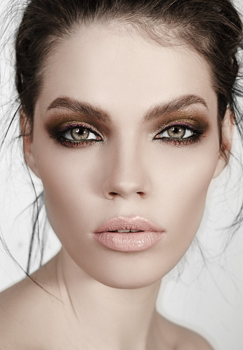 Portrait of a green eyed brunette with beautiful high-fashion make-up and beige lips on a white background.