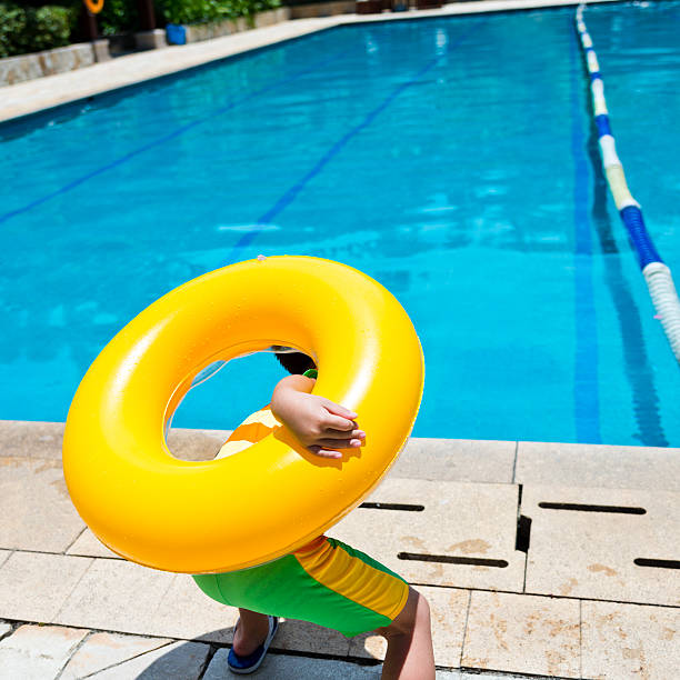 little boy standing in front of pool with a yellow swimming tube.