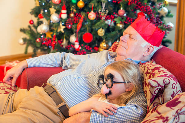 Sleeping After Christmas A little girl cuddles in to her grandfather as they both sleep on the sofa after Christmas. The little girl is wearing funny glasses and the grandad wears a party hat. sleeping grandpa stock pictures, royalty-free photos & images