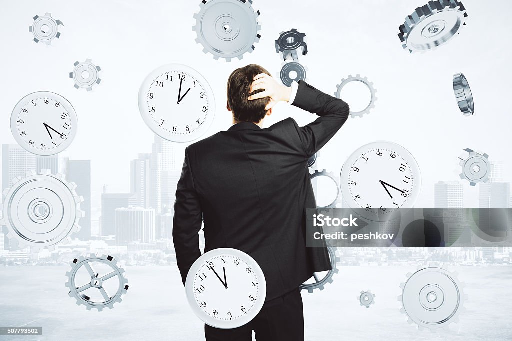 Businessman thinks about the time surrounded by clock and gears Working Late Stock Photo