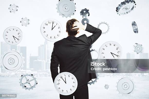 Businessman Thinks About The Time Surrounded By Clock And Gears Stock Photo - Download Image Now