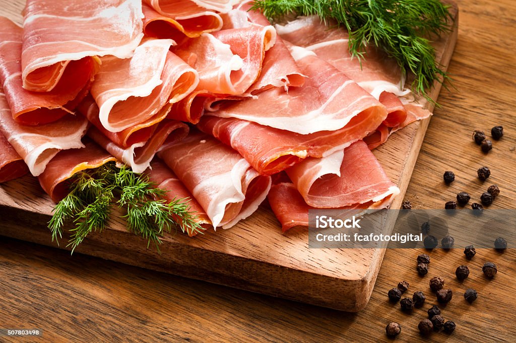 Fette di prosciutto crudo crudo sul tavolo in legno rustico - Foto stock royalty-free di Prosciutto crudo