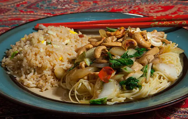 A tasty chicken and bok-choy stir-fry with cashews and red pepper on a bed of noodles, with a side of fried rice.