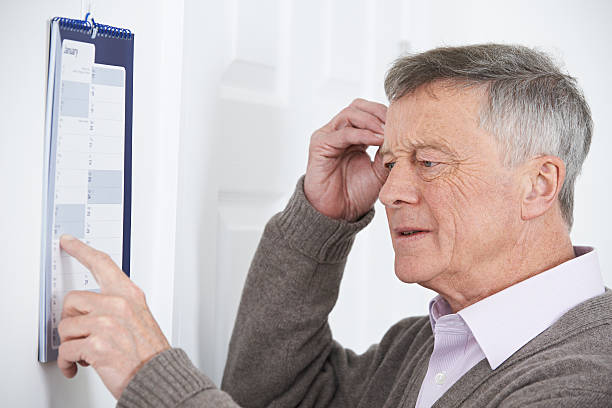 confuso uomo anziano con demenza che guarda calendario da muro - ignorance foto e immagini stock