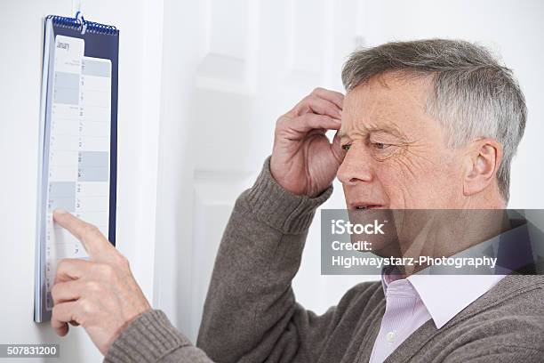 Confused Senior Man With Dementia Looking At Wall Calendar Stock Photo - Download Image Now