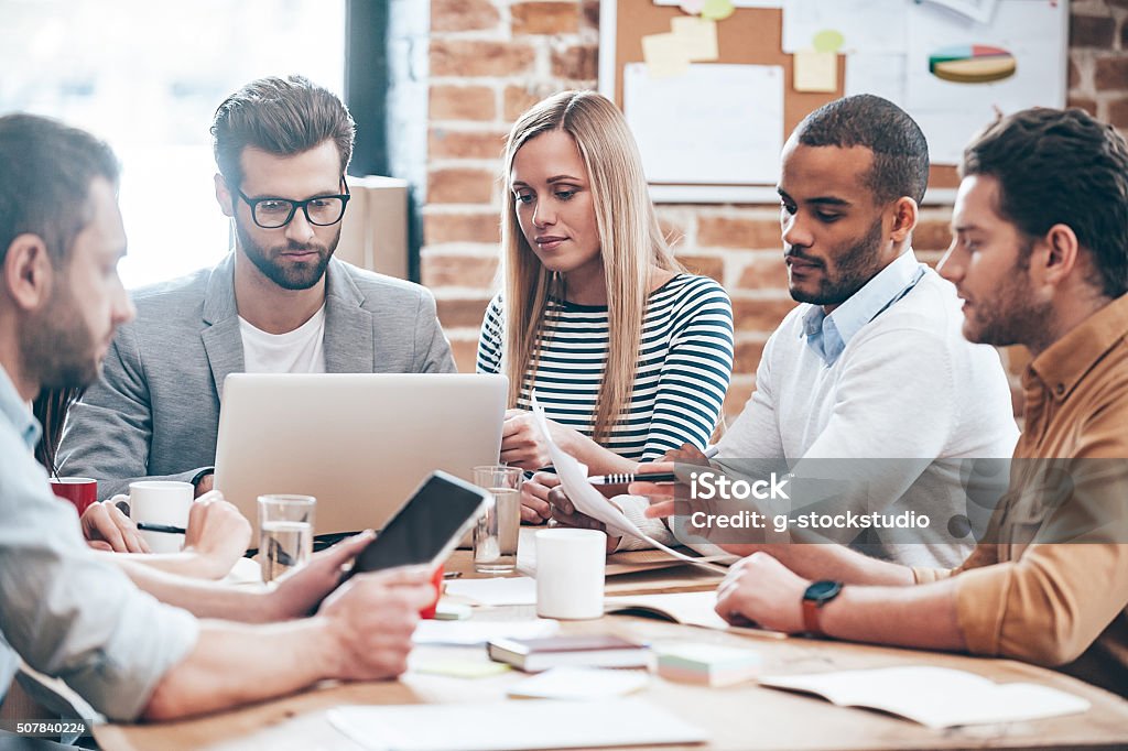 Searching for new ideas. Group of six young people reading and looking through documents while sitting at the table in office Businessman Stock Photo