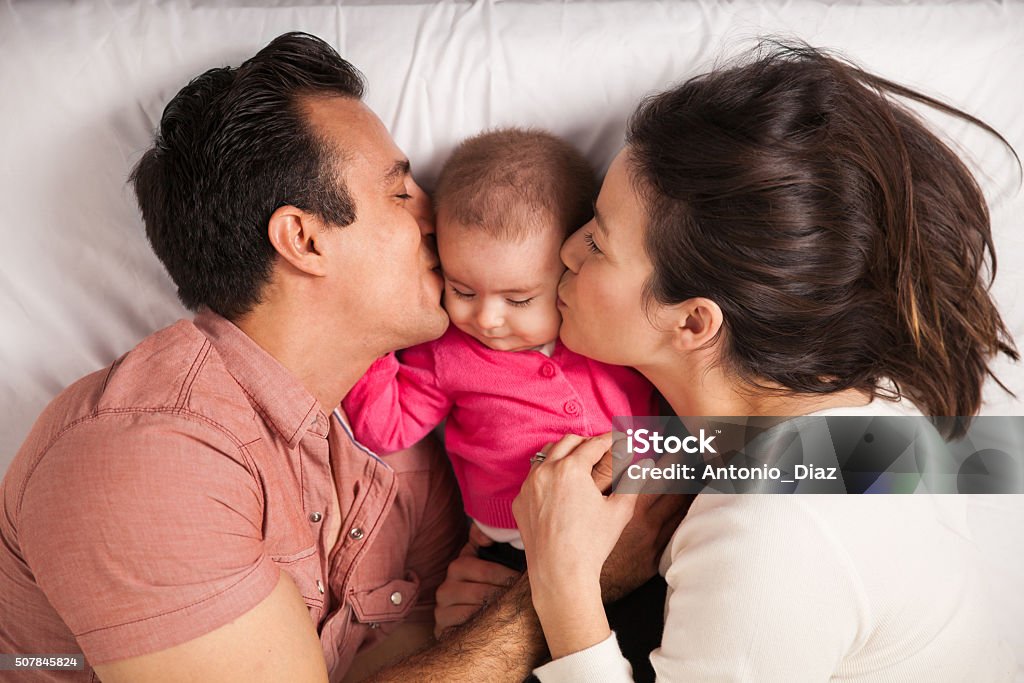 Parents in love with their baby girl Couple of new parents lying in a bed with her baby girl and kissing her both at the same time Baby - Human Age Stock Photo