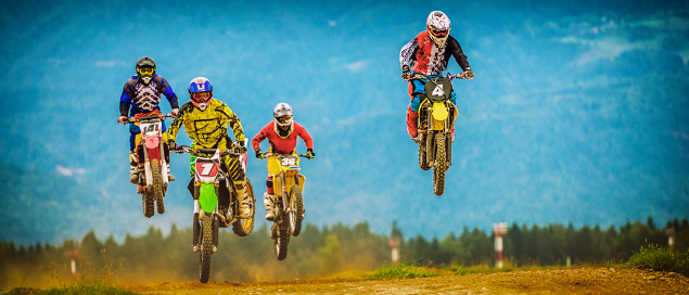 Four motocross racers in mid-air during a jump on a race track.