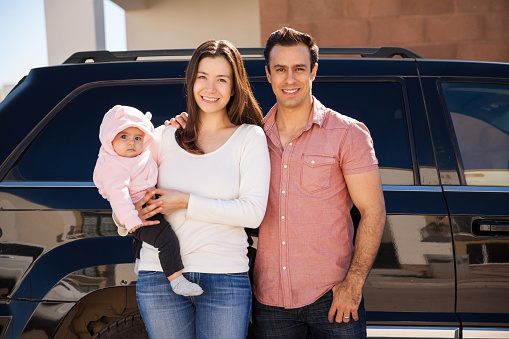 Portrait of a good looking Hispanic couple and their baby girl about to take a trip together on their car