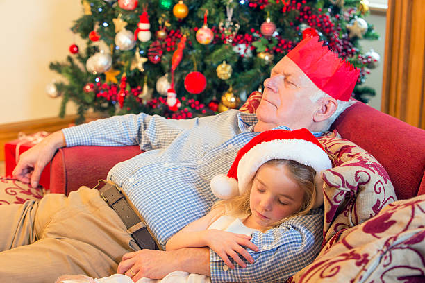 Sleeping At Christmas A little girl cuddles in to her grandfather as they sleep on the sofa after Christmas day. sleeping grandpa stock pictures, royalty-free photos & images