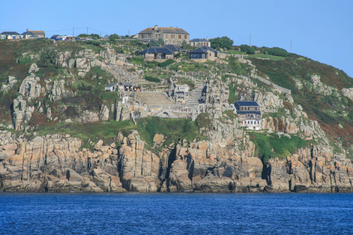 Minack Theatre, Porthcurno, Cornwall. The Minack Theatre is an open-air theatre, constructed above a gully with a rocky granite outcrop jutting into the sea. This view is taken from a boat passing the coast line.