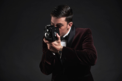 Elegant bearded professional photographer in a suit shooting with a compact DSLR camera.