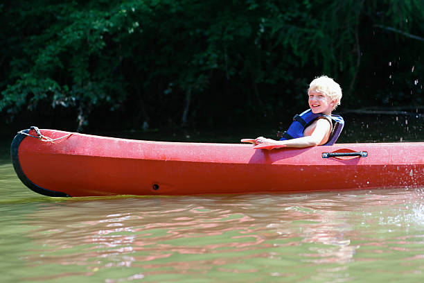 ativo menino desfrutando de caiaque no rio durante o acampamento de verão - summer camp child teenager kayak - fotografias e filmes do acervo