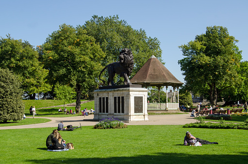 Reading, UK - September 10, 2015: People enjoying the late summer sunshine in Forbury Gardens in the centre of Reading, Berkshire.  The Maiwand Lion war memorial dominates the lawns with flower beds and trees.