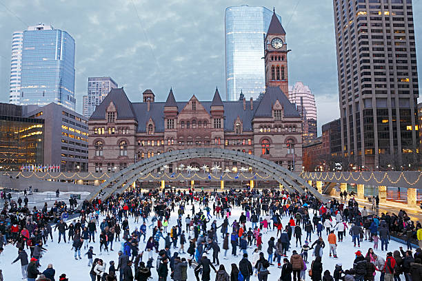 Holiday crowd ice-skating in Toronto square at dusk Holiday crowd ice-skating in Toronto's Nathan Phillips Square with Toronto City Hall and Courts plus skyscrapers in the background.  The ice skating rink is adorned with Christmas and New Year decorations.  Moody sky.  Horizontal, copy space, small amount of noise evident due to 800ISO. new year urban scene horizontal people stock pictures, royalty-free photos & images