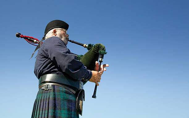 piper odtwarzanie bagpipes szkockich kilt przeciw błękitne niebo - scottish music zdjęcia i obrazy z banku zdjęć