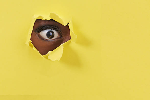A close-up moment of pure curiosity as a 10-year-old child peeks through a torn yellow paper. The child's expression conveys a sense of wonder and exploration.