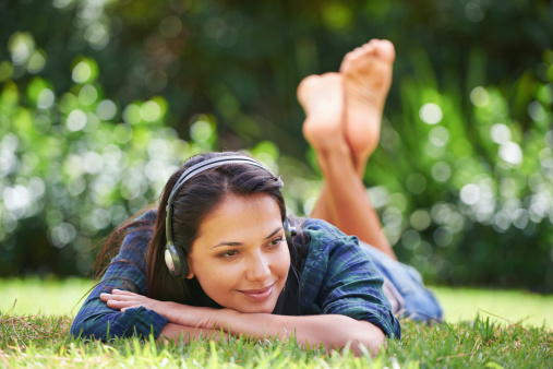 Shot of an attractive young woman lying on the grass and listening to music