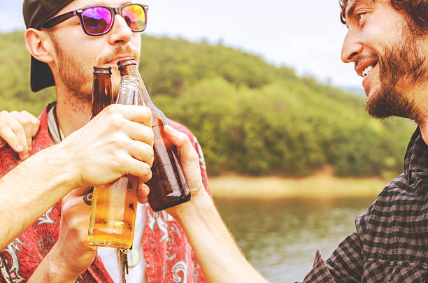 summer, holidays, vacation, happy people concept - group of friends having fun on the beach with bottles of beer or non-alcoholic drinks