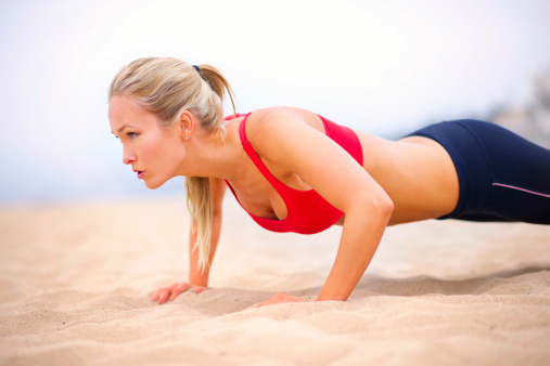 A young woman doing push ups on the beach in sportswear