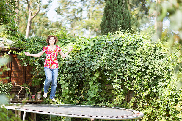 cheerful senior woman having fun jumping on trampoline, outdoors in summer