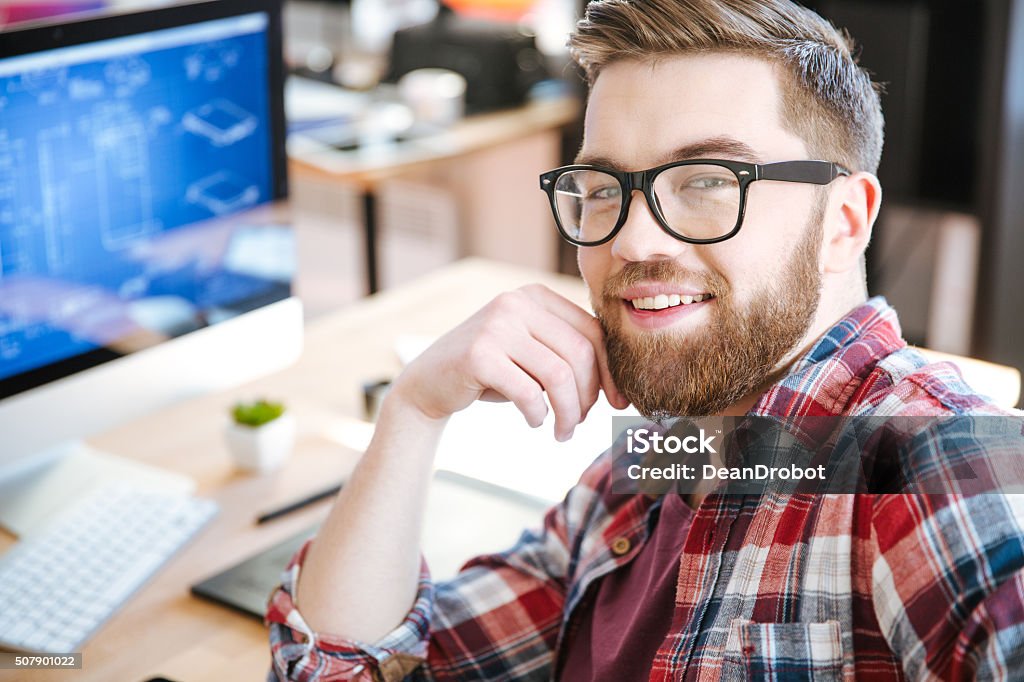 Happy attractive man working and designing project on computer Happy attractive young man with beard in glasses working and designing project on his computer Adult Stock Photo