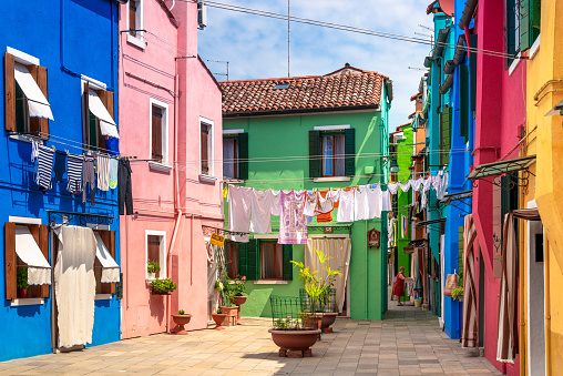 Burano, Italy - June 28, 2014: Senior woman hanging laundry on clothes line, colorful apartment buildings in village of Burano near Venice, Italy.