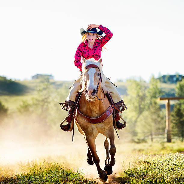 Cowgirl riding as fast as the wind on a ranch and holding on to her hat for dear life.
