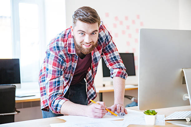 istock Smiling bearded man standing and working on blueprint in office 507902126