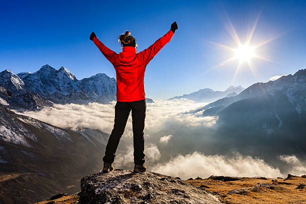 Woman lifts her arms in victory, Mount Everest National Park Young woman, wearing red jacket, lifts her arms in victory. She is standing on the top of a mountain and watching sunset over Himalayas .Mount Everest National Park. This is the highest national park in the world, with the entire park located above 3,000 m ( 9,700 ft). This park includes three peaks higher than 8,000 m, including Mt Everest. Therefore, most of the park area is very rugged and steep, with its terrain cut by deep rivers and glaciers. Unlike other parks in the plain areas, this park can be divided into four climate zones because of the rising altitude.http://bem.2be.pl/IS/nepal_380.jpg solu khumbu stock pictures, royalty-free photos & images