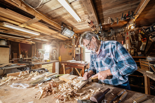 Senior carpenter standing in his workshop, working on a piece of wood with his chisel. Nova Scotia, Canada.