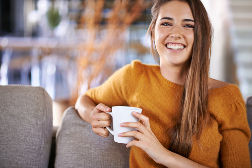 Cropped image of a pretty young female drinking coffee while sitting on the sofa