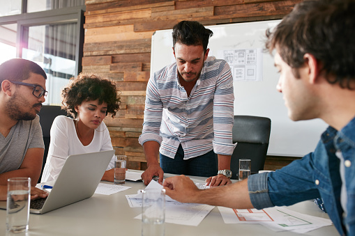 Young man discussing market research with colleagues in a meeting. Team of young professionals having a meeting in conference room looking at documents.