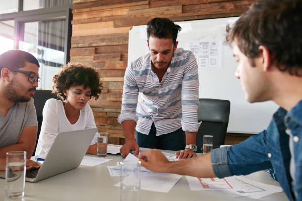 Young man discussing market research with colleagues Young man discussing market research with colleagues in a meeting. Team of young professionals having a meeting in conference room looking at documents. job placement stock pictures, royalty-free photos & images