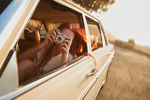 Shot of  young woman taking photos while sitting in a car. Female capturing a perfect road trip moment.