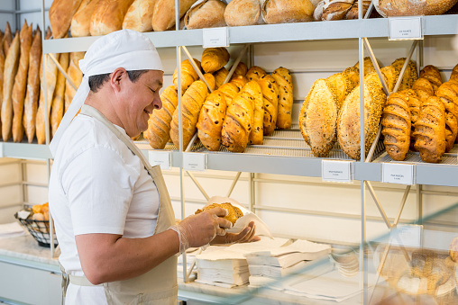 Baker working at the bakery putting fresh bread into display at the shop