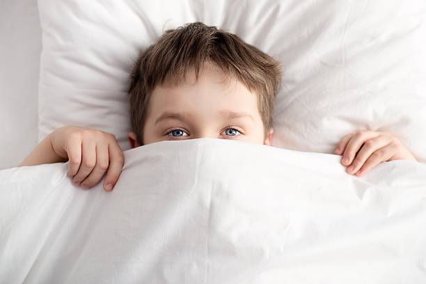 istock little boy in bed covering his face with white blanket 507970160
