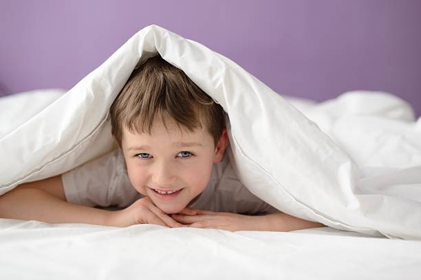 boy hiding in bed under a white blanket or coverlet