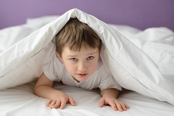 istock 7 years old boy hiding in bed 507972202