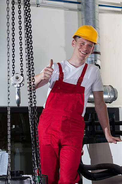 Blue-collar worker standing near to lifting equipment and showing thumbs up sign