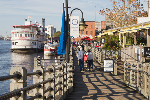Wilmington, North Carolina, USA-November 13, 2015: The downtown boardwalk on Water Street with tour boats, restaurant, and tourists by the Cape Fear Landing off Orange Street