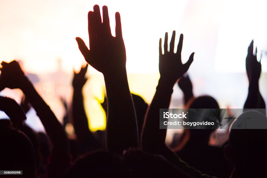 crowd A crowd level view of hands raised from the spectating crowd interspersed by colorful spotlights and a smokey atmosphere Congregation Stock Photo