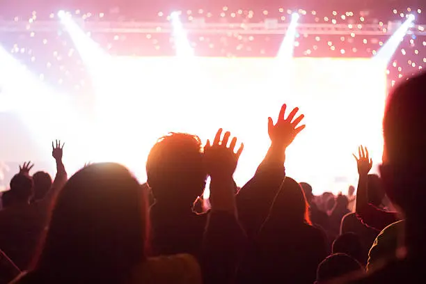 A crowd level view of hands raised from the spectating crowd interspersed by colorful spotlights and a smokey atmosphere