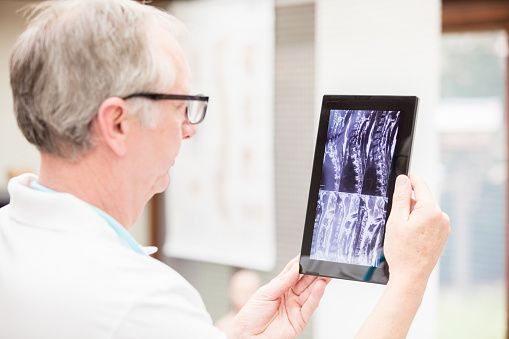 A mature male doctor, checking some MRI images of the neck on tablet PC. Image taken with Canon EOS 5 Ds and EF 70-200mm 2,8 USM L.