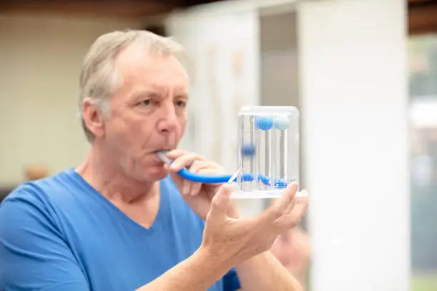 A male person, performing a simple lung function test by using a triflow. He has to blow into the tube, so the balls in the device lift a little bit according to the power of his breath.