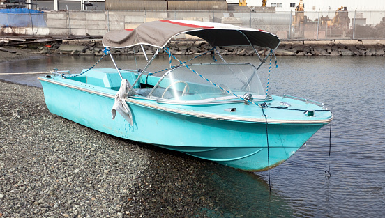 Deserted blue motor boat on bay shore. Horizontal.