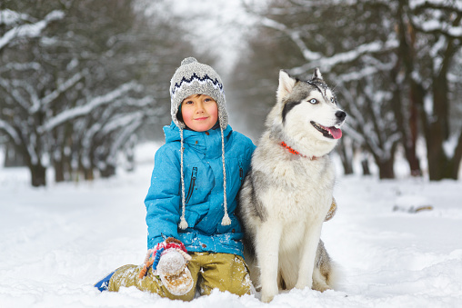 happy boy hugging dog or husky outdoors in winter day.