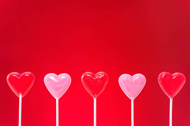 A row of five pink and red heart shaped lollipops, on red background for Valentine's day.